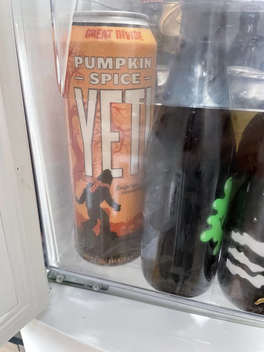Burk med Pumpkin Spice Yeti öl i ett kylskåp, flankerad av andra flaskor och burkar.
