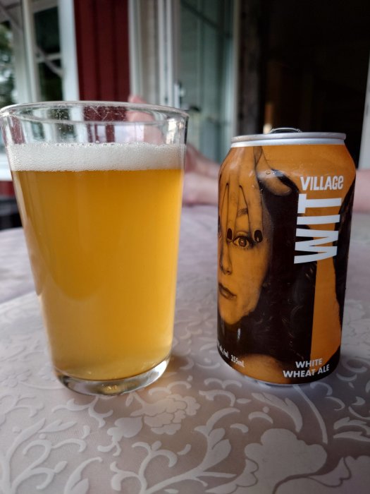 Ett glas med veteöl bredvid en burk öl på ett mönstrat bord.