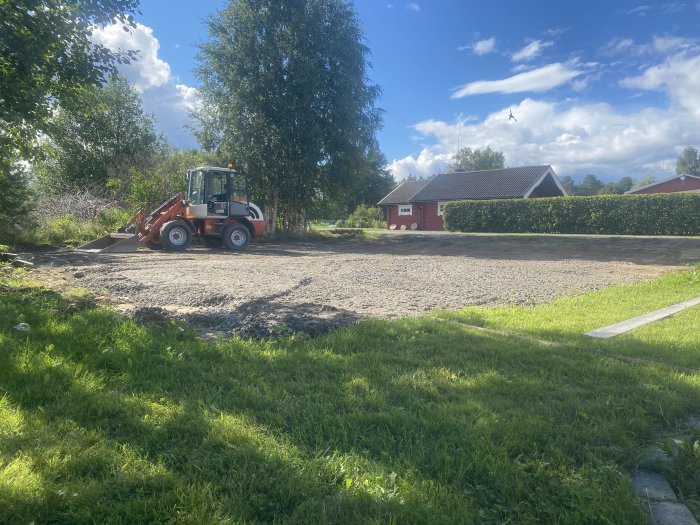 En grävmaskin på en gruslagd tomt vid förberedelsearbeten för garagetillbyggnad.