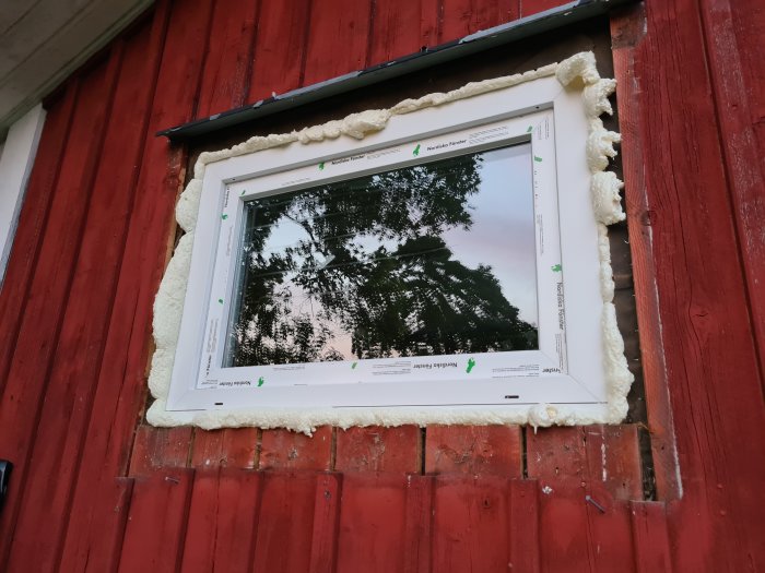 Nytt fönster installerat i röd trävägg, fastsatt med expanderande byggskum