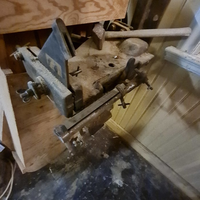 Gammal arbetsbänk med skruvstycken och verktyg i ett dammigt hörn av ett verkstadsrum.