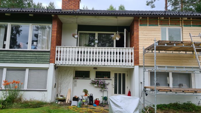 Renovering pågår på en tvåvåningshusfasad med byggställningar och ny kledning.