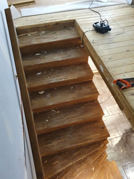 Orenoverad trätrappa med spån och verktyg under renoveringsprocessen.