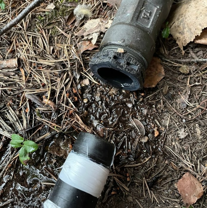 Reparerad avloppsrör med tejp på marken bland löv och barr.