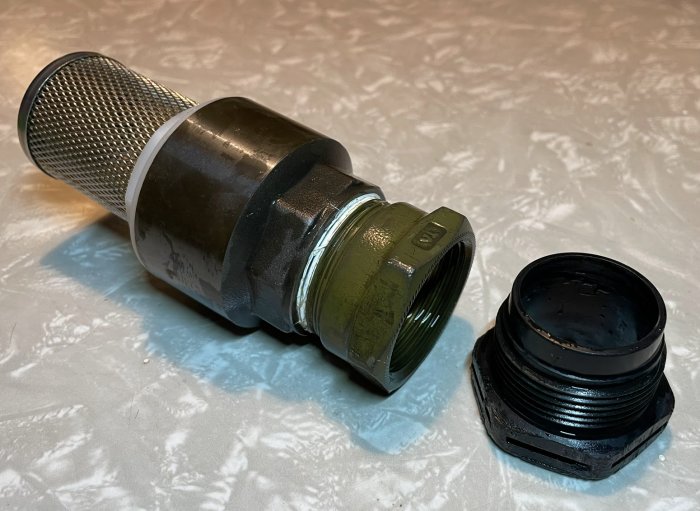 Rörkoppling med metallnät, kompensationshylsa och svart tryckskruv på en yta.