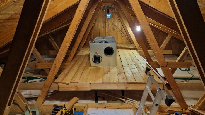 Aggregatet installerat på vind med synliga takstolar och isolering, verktyg i förgrunden.