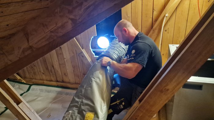Person installerar isolering i ett vindutrymme vid en vindslucka.