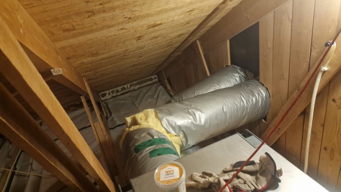 Ventilationskanaler i isolering på en vind med öppen takstol och synliga träelement.