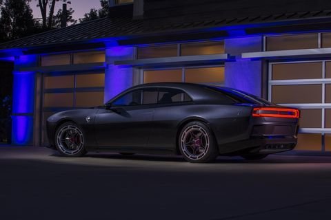 Dodge Charger parkerad framför garage i skymningen, med belysning som framhäver dess konturer.