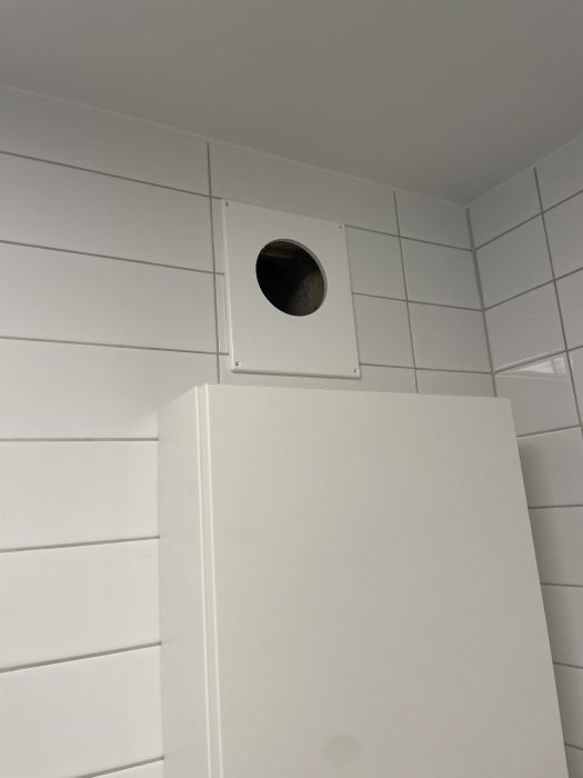 Väggventil ovanför en badrumsskåp mot en kaklad vägg.