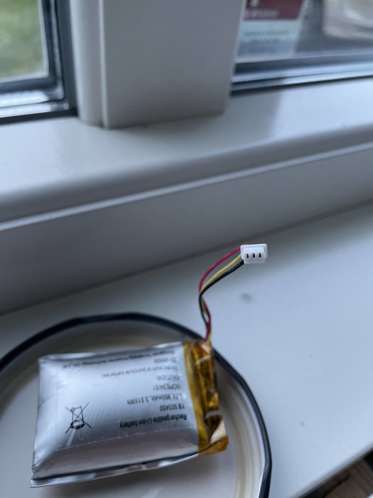 Swollen lithium-ion battery with exposed wires on a window sill.