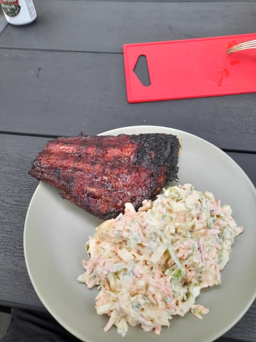 Ribs med krispig yta på tallrik bredvid en sallad av coleslaw, på ett mörkt träbord.