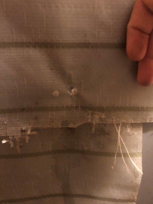 Närbild på vattenskada i tak med synliga droppar och fläckar, pekfingret pekar på skadan.