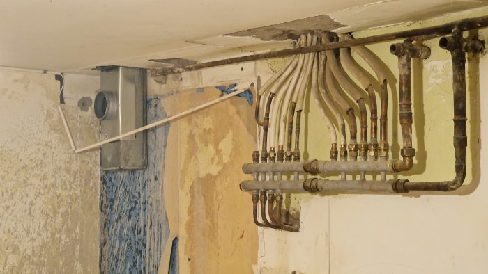 Installation av ventilation och rörarbeten i ett renoveringsprojekt med synliga gamla rör och sladdar.