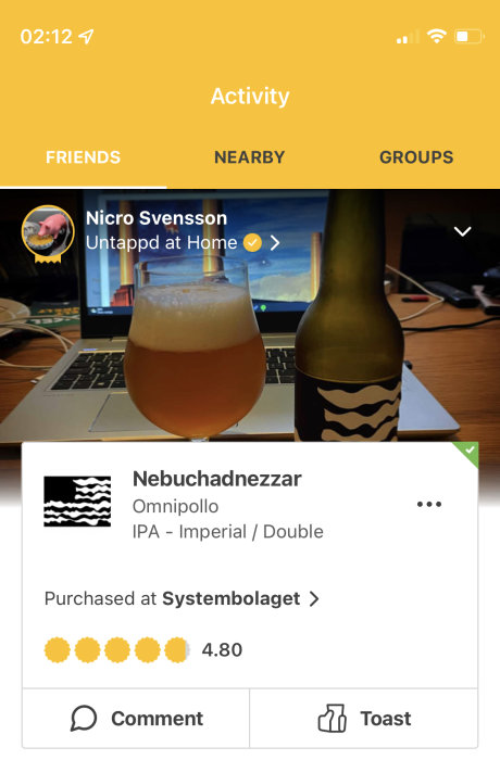 Ölglas fyllt med skummande öl framför en öppen dator och en ölflaska från Omnipollo.