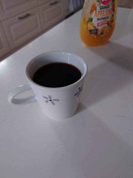 Kaffekopp med svart kaffe och en flaska apelsinjuice på ett köksbord.