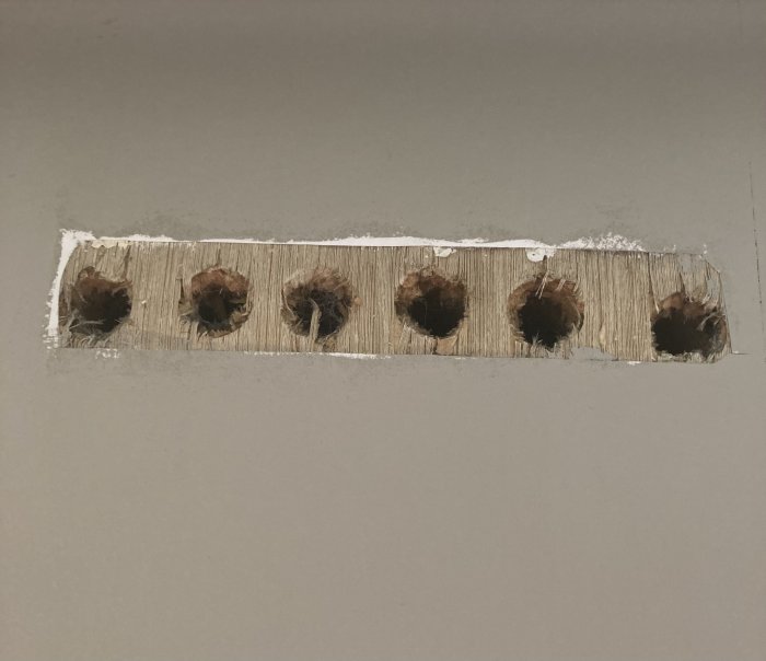 En rad med borrhål i en vägg, täckta av damm och spån, förberedda för elinstallation.