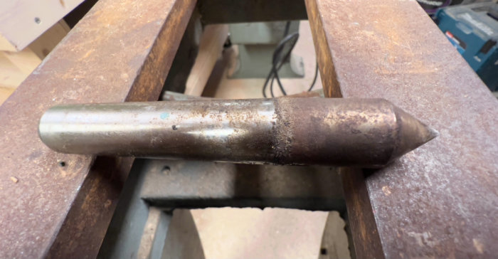 Metallstång på en arbetsbänk med synlig slitage och rost, använd i reparation av gammal svarv.