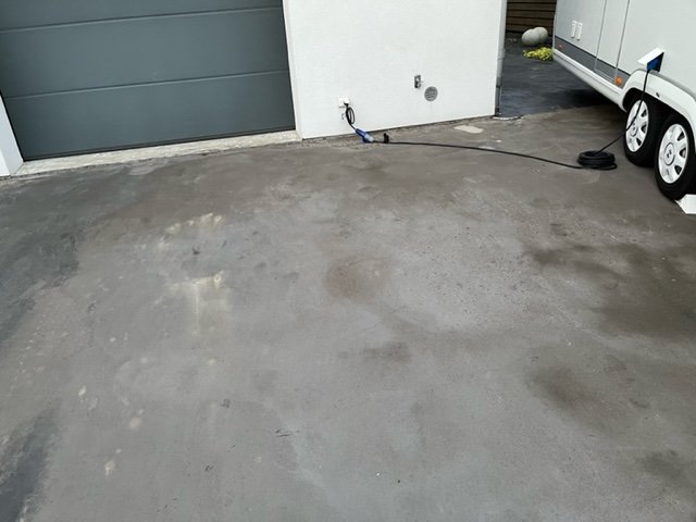 Nyuppgjuten betonginfart med slitage och fläckar framför garageport och del av släpvagn synlig.