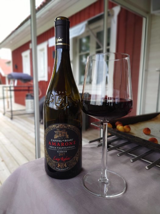 Flaska Amarone-vin och ett glas med rött vin på ett bord med hus i bakgrunden.