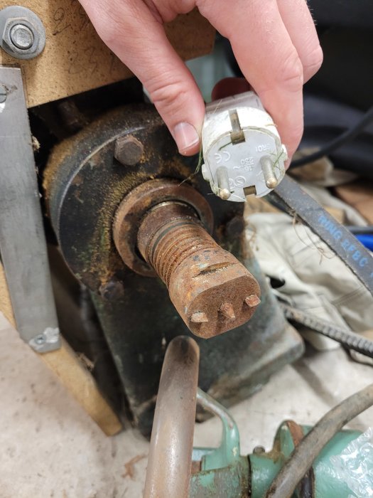 Hand håller mätverktyg bredvid rostig bult, med möjlig storlek M32, i verkstadsmiljö.