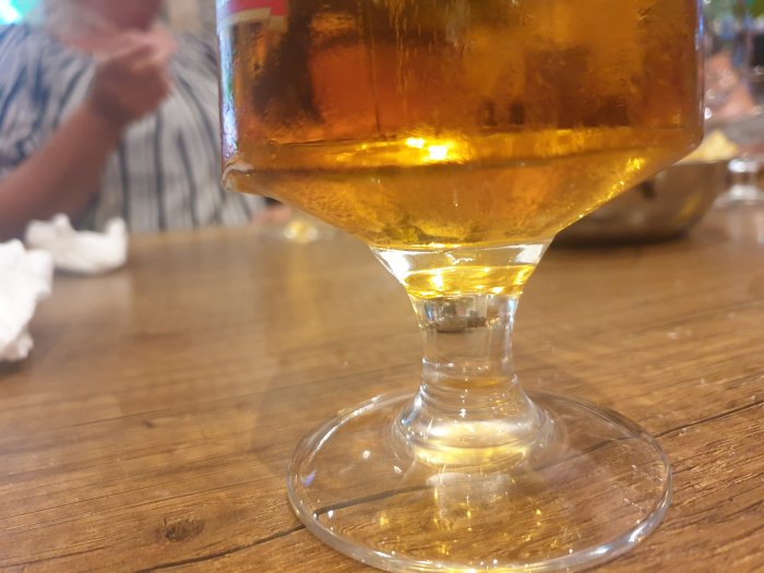 Närbild på ett ölglas med tydlig kant på foten stående på ett träbord.