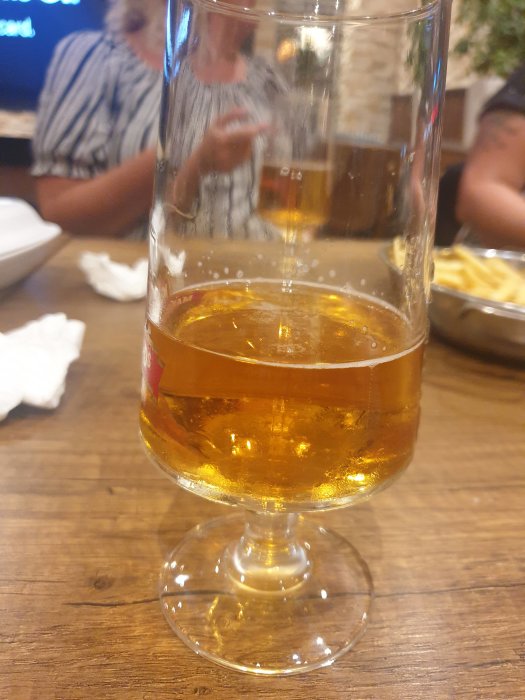 Ölglas fyllt med öl står på bord, synlig kant under glasets botten noterad.