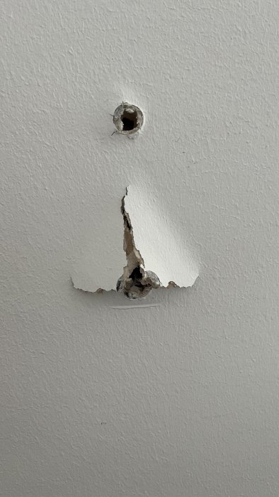 Skadad vit vägg med borrat hål och sprucken puts runtomkring.