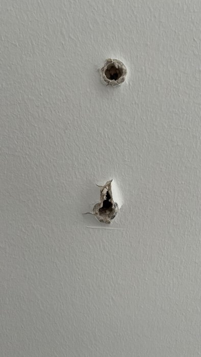 Två hål i en vit vägg varav det nedre är större och oregelbundet.