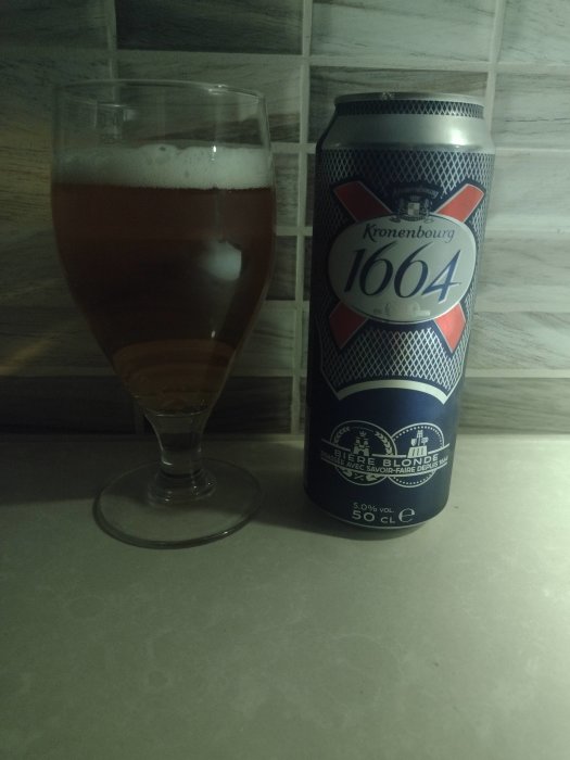 Ett glas öl bredvid en Kronenbourg 1664 ölburk på en köksbänk.