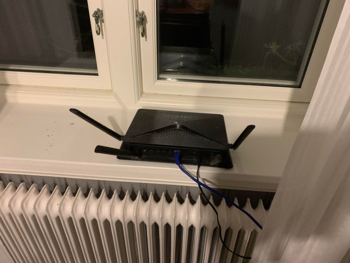 Svart router med två antenner på ett fönsterbräde ovanför en vit elementradiator.