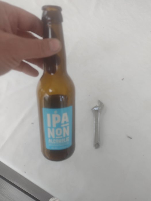 Flaska med alkoholfri IPA öl och en skiftnyckel på ett vitt bord.