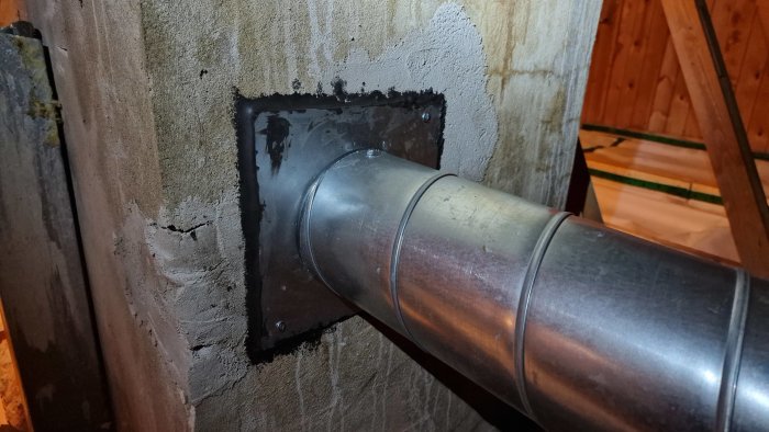Ventilationsrör av metall genomför en brandisolerad genomföring i en murstock med spackel och pannkitt runtom.