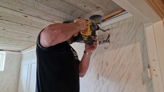 Person använder en gult och svart skruvdragare för att fästa något i ett träbjälklag.