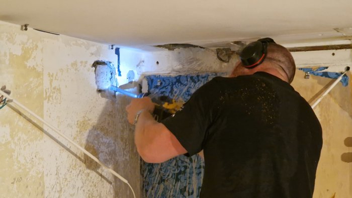 Person som borrar genom vägg i renoveringsprojekt med skyddshörselkåpor.