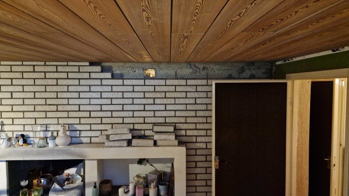 Renoverat rum med träpaneltak, vitt tegelliknande kakel och nymålad altandörr.