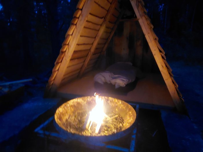 Träkoja med öppen front och eldstad vid natt för glamping-upplevelse.