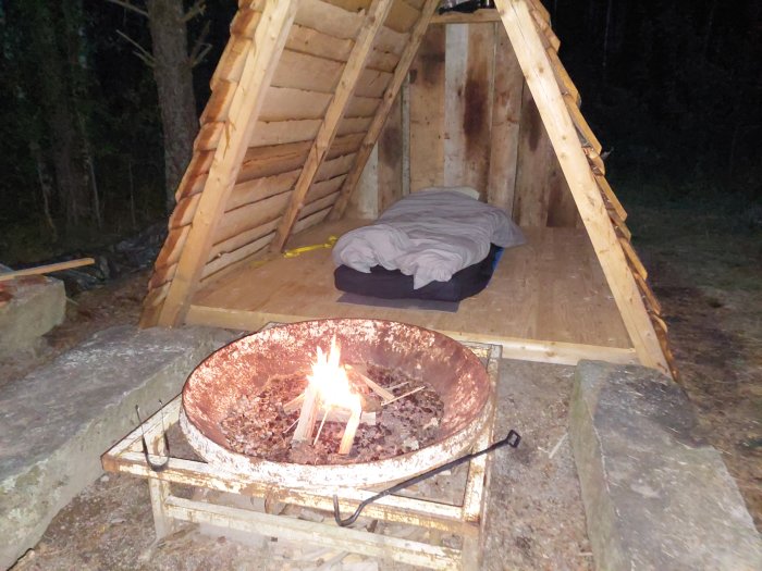 Glamping med tältkonstruktion i trä och tänd eld i brandgrop på natten.