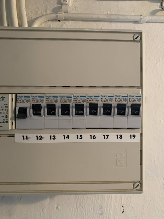 Elskåp med öppen dörr som visar säkringar och etiketter märkta 11 till 19 i ett gammalt hus.