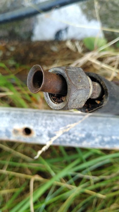 Närbild av en rostig rörkoppling på en metallstolpe med gräs i bakgrunden