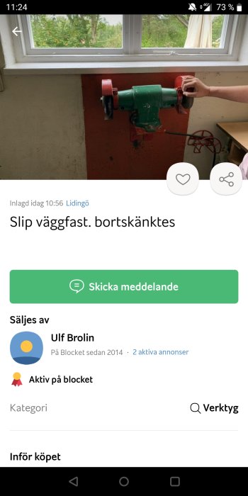 Väggmonterad slipmaskin med röd slipskiva och någons hand som rör vid slipmaskinen.