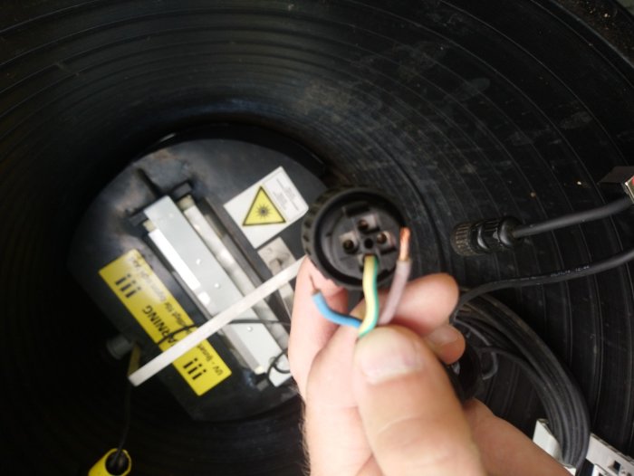 Hand håller en elektrisk koppling med kablar framför luftvärmepump.
