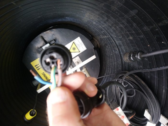 Elektriska kablar och kontakter med öppen ände mot bakgrunden av svart spiralkabel och apparat.