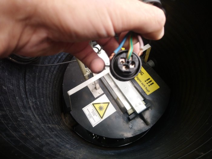 Hand håller en elektrisk kontakt ovanför en cirkulär sågenhet.