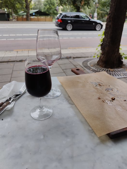 Ett glas Lambrusco-vin på ett bord utomhus bredvid en tom glas och matrester.
