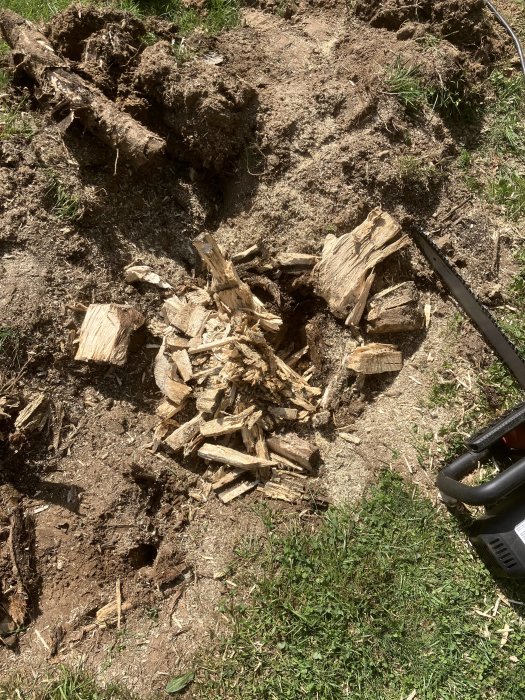 Flismaskin bredvid en hög med flisade träbitar vid en grävd grop där en stubbe har tagits bort.