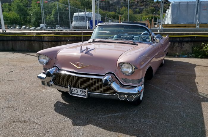 En rosa Cadillac cabriolet från 1950-talet parkerad utomhus i dagsljus.