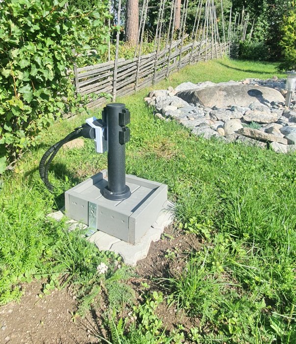 Installation av 4vägs strömlåda i trädgård med kabelskydd och kablar synliga i grästäckt område.
