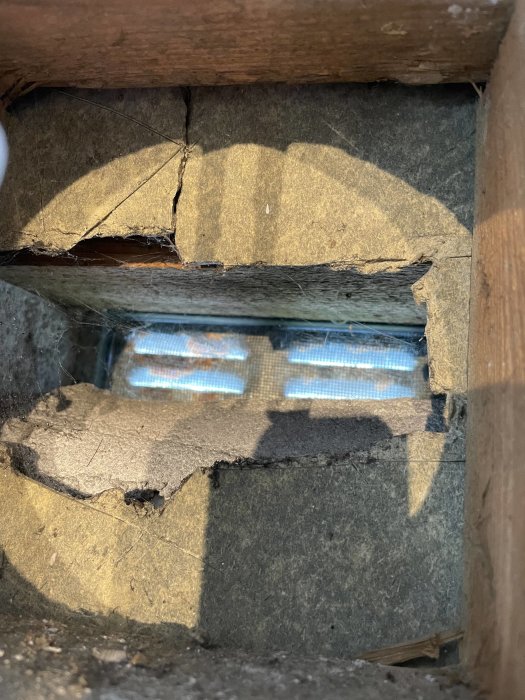 Hål i isoleringen mellan takbjälkar med synligt dagsljus igenom.