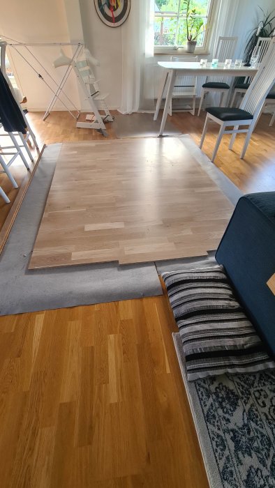Delvis monterat ljust träparkettgolv bredvid ett färdigt mörkare parkettgolv i ett vardagsrum.